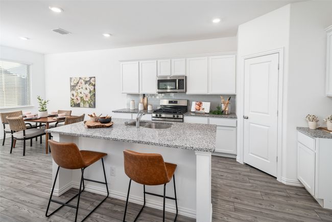 Kitchen featuring appliances with stainless steel finishes, a sink, wood finished floors, a breakfast bar, and white cabinetry | Image 7