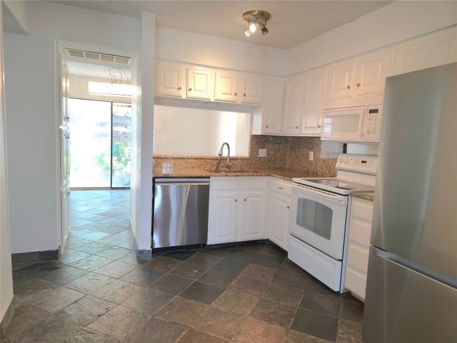 Kitchen featuring stainless steel appliances, stone tile floors, tasteful backsplash, and white cabinets | Image 4