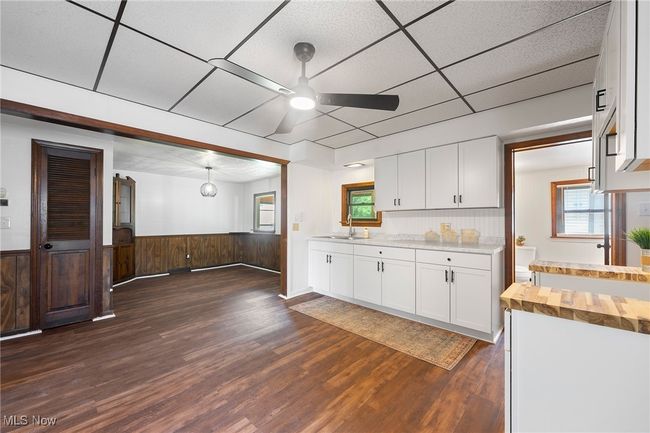 Kitchen with ceiling fan, butcher block counters, dark wood-type flooring, white cabinets, and a wainscoted wall | Image 9