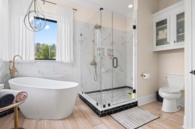 Bathroom featuring toilet, a freestanding tub, a marble finish shower, tile walls, and a chandelier | Image 20