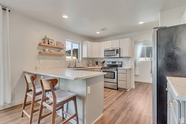 Kitchen featuring appliances with stainless steel finishes, a peninsula, backsplash, light wood-type flooring, and recessed lighting | Image 10