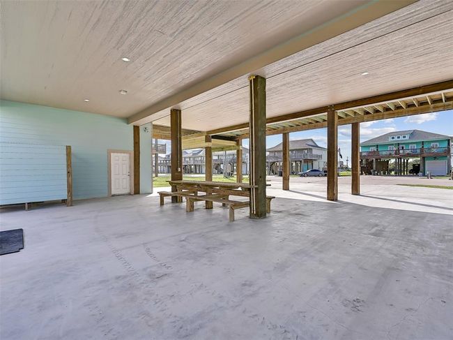 The ground-level features a single-bay garage for storage plus a spacious covered area with an enclosed outdoor shower and a built-in picnic table with benches—ideal for outdoor games, dining, or shaded relaxation after a day at the beach. | Image 27