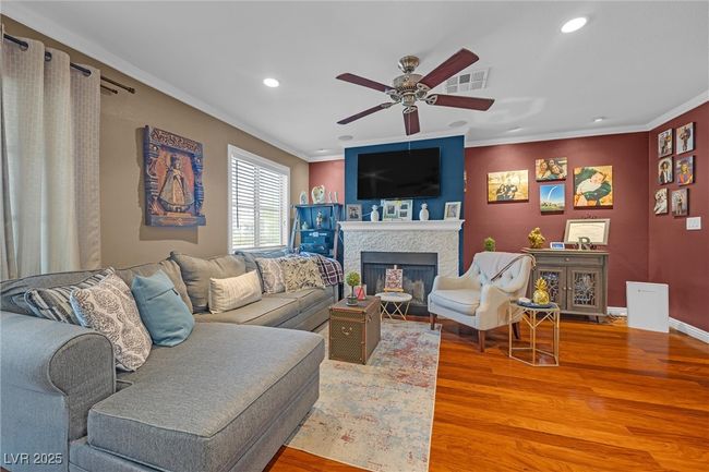 Living room featuring a ceiling fan, light wood finished floors, a fireplace with flush hearth, visible vents, and ornamental molding | Image 12