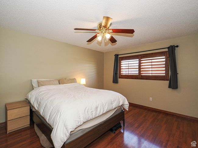 Bedroom with wood finished floors, baseboards, a textured ceiling, and a ceiling fan | Image 19
