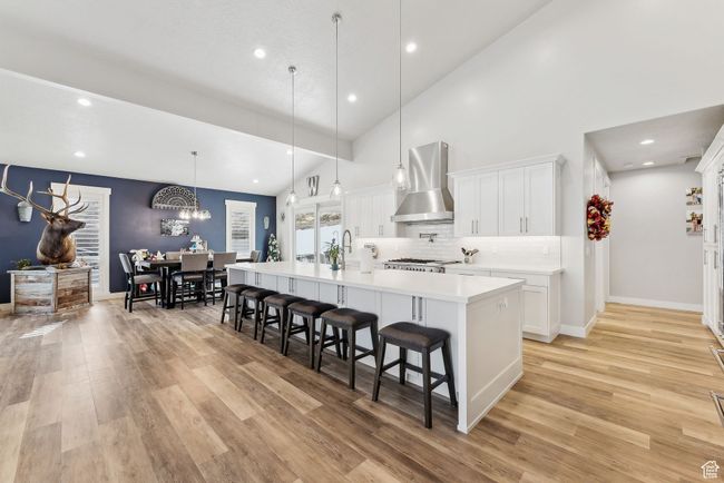 Kitchen with wall chimney range hood, a spacious island, light countertops, a kitchen bar, and light wood-type flooring | Image 36