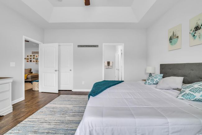 Bedroom featuring a ceiling fan, dark wood-style floors, ensuite bathroom, and a raised ceiling | Image 31