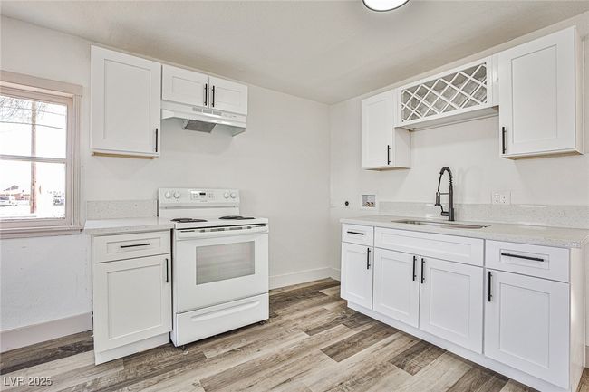 Kitchen with white electric range, under cabinet range hood, white cabinetry, and light wood finished floors | Image 4