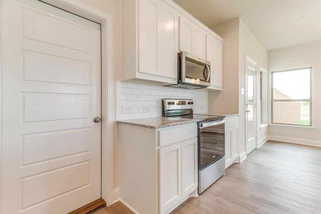 Kitchen with tasteful backsplash, white cabinetry, light stone counters, stainless steel appliances, and light hardwood / wood-style flooring | Image 14