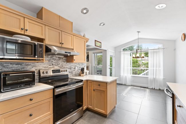 Kitchen with appliances with stainless steel finishes, under cabinet range hood, vaulted ceiling, light countertops, and decorative backsplash | Image 8
