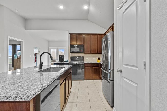 Kitchen with black appliances, a sink, lofted ceiling, backsplash, and light stone counters | Image 15