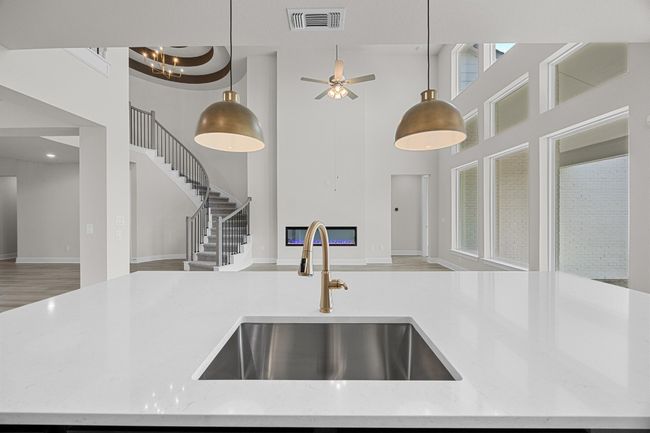 Kitchen with a sink, open floor plan, a towering ceiling, decorative light fixtures, and light stone counters | Image 11