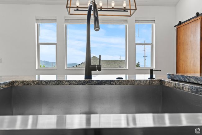 Kitchen view of dark stone countertops, a barn door, a sink, and hanging light fixtures | Image 9