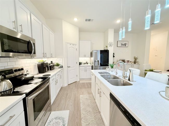 Kitchen featuring stainless steel appliances, light wood finished floors, light countertops, decorative backsplash, and white cabinets | Image 4