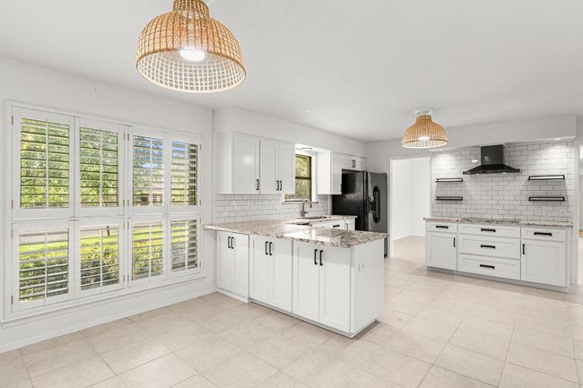 Kitchen featuring wall chimney exhaust hood, decorative backsplash, white cabinets, black fridge with ice dispenser, and a peninsula | Image 14