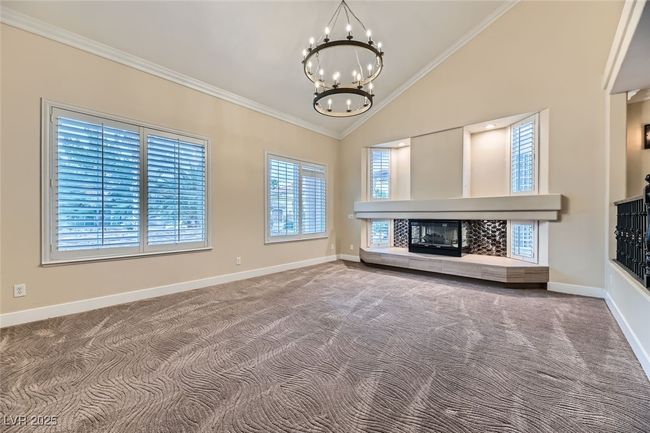 Unfurnished living room featuring a chandelier, carpet, crown molding, a fireplace, and high vaulted ceiling | Image 9