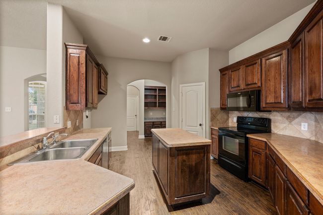 Kitchen featuring arched walkways, visible vents, a sink, and black appliances | Image 12