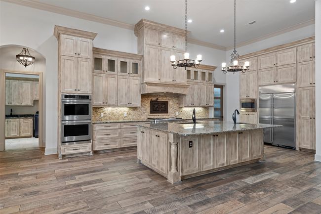 Kitchen featuring light brown cabinetry, a sink, built in appliances, a chandelier, and a center island with sink | Image 11