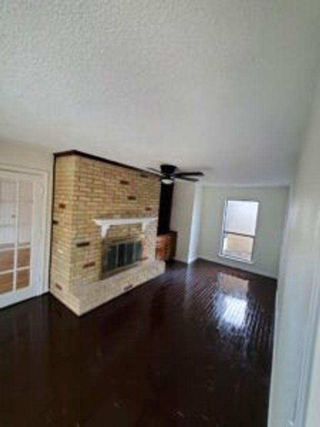 Unfurnished living room with dark wood-type flooring, a brick fireplace, a textured ceiling, and ceiling fan | Image 23