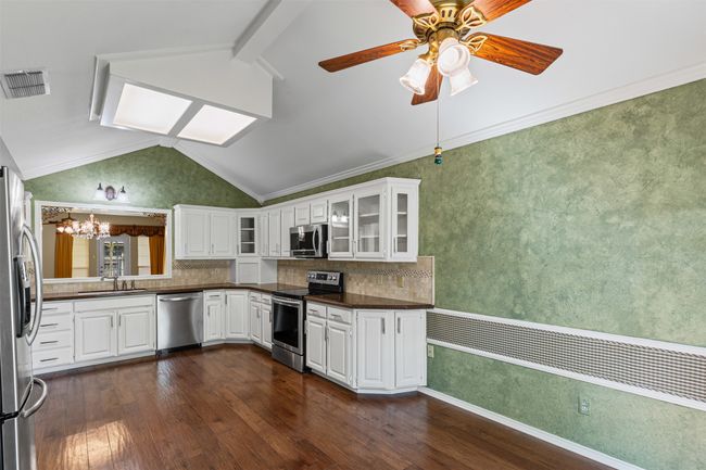 Kitchen featuring stainless steel appliances, dark countertops, dark wood-type flooring, lofted ceiling, and a chandelier | Image 7