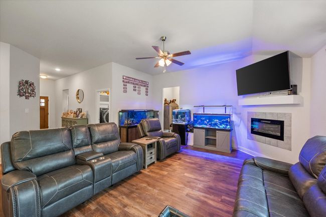 Living room with a ceiling fan, wood finished floors, and an electric fireplace. | Image 5
