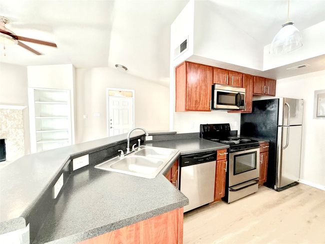 Kitchen with lofted ceiling, stainless steel appliances, light wood finished floors, ceiling fan, and a peninsula | Image 5