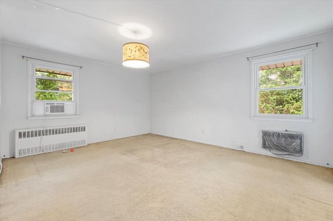 Spare room featuring radiator heating unit, carpet floors, and an AC wall unit | Image 7