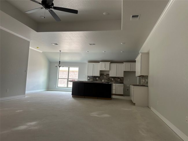 Kitchen featuring concrete floors, a kitchen island, white cabinetry, visible vents, and decorative backsplash | Image 7