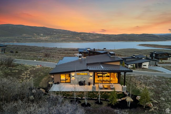 Back of property at dusk featuring stone siding, a standing seam roof, metal roof, and a water and mountain view | Image 9