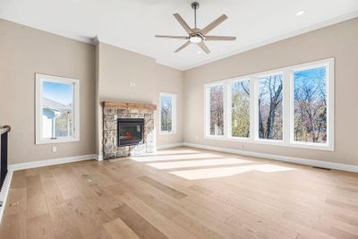 Unfurnished living room featuring a stone fireplace, light wood-type flooring, ceiling fan, and ornamental molding | Image 2