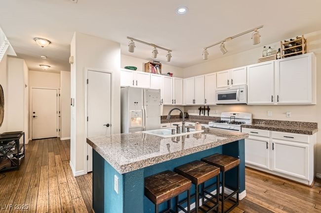 Kitchen featuring white cabinetry, a kitchen bar, white appliances, a sink, and hardwood / wood-style flooring | Image 7
