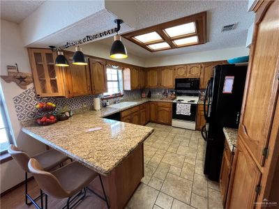 Kitchen featuring pendant lighting, kitchen peninsula, backsplash, black appliances, and a breakfast bar area | Image 2