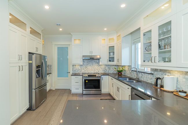 Kitchen with stainless steel appliances, a sink, under cabinet range hood, wood finished floors, and white cabinetry | Image 7
