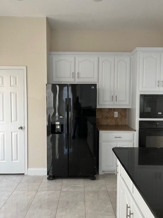 Kitchen featuring black refrigerator with ice dispenser, oven, dark countertops, white cabinetry, and tasteful backsplash | Image 12