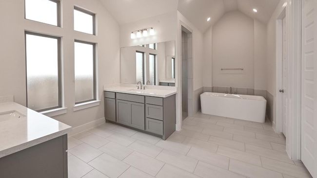 Full bath featuring vaulted ceiling, a freestanding bath, two vanities, light tile patterned flooring, and recessed lighting | Image 11