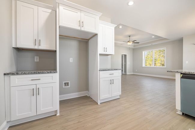Kitchen featuring white cabinetry, ceiling fan, light hardwood / wood-style flooring, stainless steel dishwasher, and a tray ceiling | Image 11
