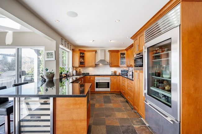 Kitchen featuring stainless steel appliances, wall chimney range hood, a peninsula, brown cabinets, and dark countertops | Image 10