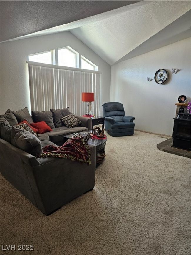 Carpeted living room with lofted ceiling, a wood stove, and a textured​​‌​​​​‌​​‌‌​‌‌​​​‌‌​​‌‌​‌​​​​​‌ ceiling | Image 9