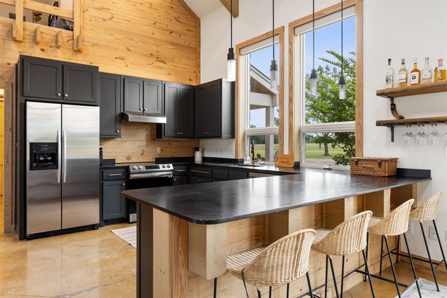 Kitchen with stainless steel appliances, dark countertops, a peninsula, a towering ceiling, and under cabinet range hood | Image 14