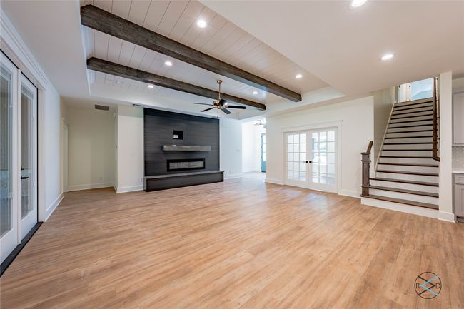 Unfurnished living room with a large fireplace, light hardwood / wood-style flooring, beam ceiling, and french doors | Image 10
