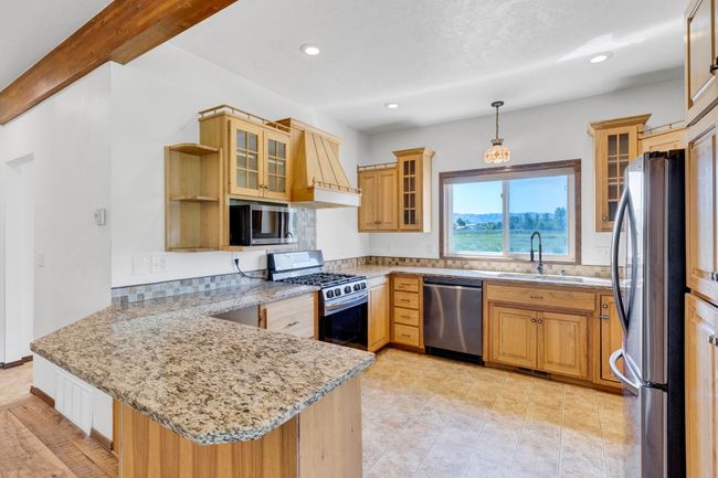 Kitchen featuring stainless steel appliances, a sink, a peninsula, custom exhaust hood, and light stone counters | Image 21