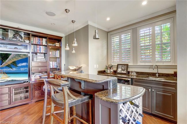 Bar with light wood-style floors, indoor wet bar, ornamental molding, a sink, and pendant lighting | Image 14