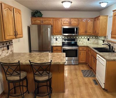 Kitchen with sink, a textured ceiling, appliances with stainless steel finishes, a kitchen breakfast bar, and light hardwood / wood-style floors | Image 2