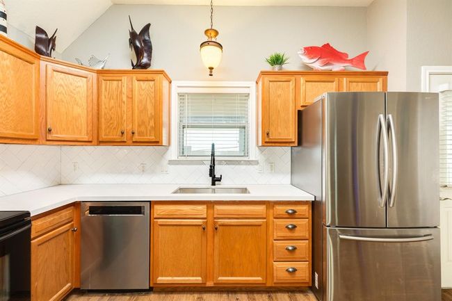 This kitchen features window over the sink for sunset and bay side views, and a modern faucet. Accents include decorative fish and a hanging light fixture, with a window for natural light. | Image 11