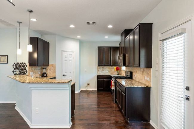 Kitchen featuring appliances with stainless steel finishes, a peninsula, light stone counters, dark wood finished floors, and decorative backsplash | Image 22