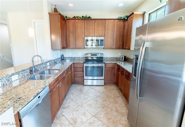 Kitchen with brown cabinets, appliances with stainless steel finishes, a sink, and light stone countertops | Image 11