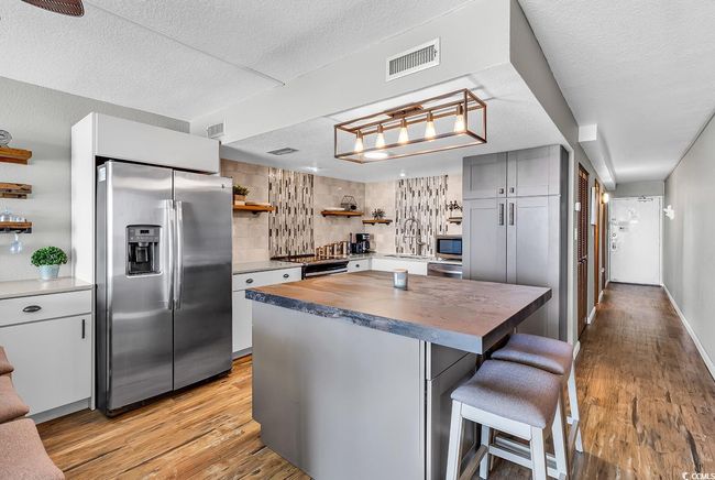 Kitchen with butcher block counters, open shelves, stainless steel appliances, light wood finished floors, and visible vents | Image 15