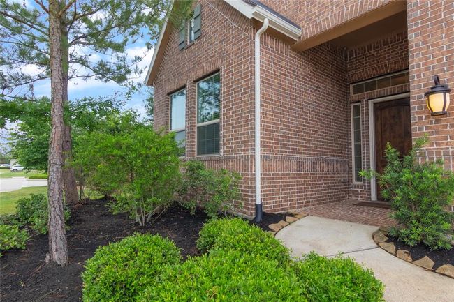This photo showcases the inviting entrance of a brick home, featuring a well-maintained walkway and lush landscaping with shrubs and trees. The presence of a stylish outdoor light adds charm to the entryway. | Image 5