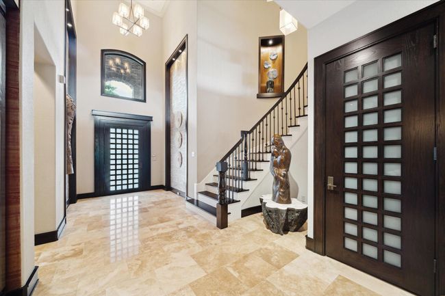 From the moment you step inside, this stunning foyer blends architectural elegance with curated design. The open layout is accented by lighted art niches, a curved staircase with wrought iron spindles, and a curved inset perfect for showcasing a sculptural centerpiece that adds gallery-like elegance. Thoughtful architectural lighting highlights the textures and finishes throughout, while an upper gallery and large arched window invite natural light into this truly unforgettable space. | Image 6