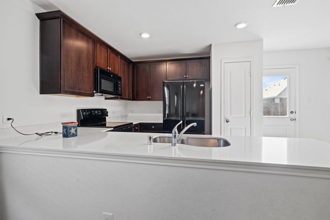 Kitchen featuring black appliances, dark brown cabinets, a sink, and light countertops | Image 5