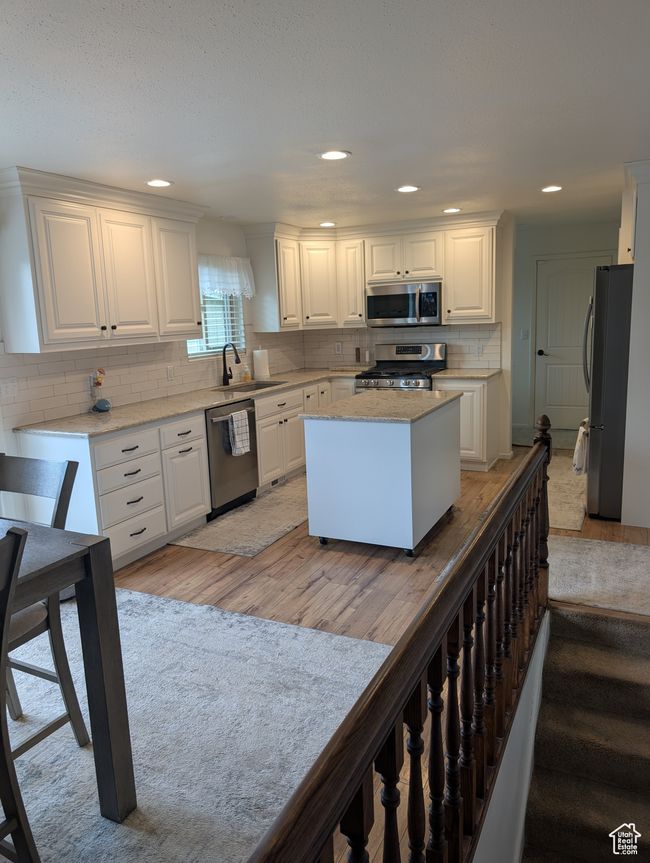 Kitchen with appliances with stainless steel finishes, a sink, light wood-style flooring, white cabinetry, and tasteful backsplash | Image 7